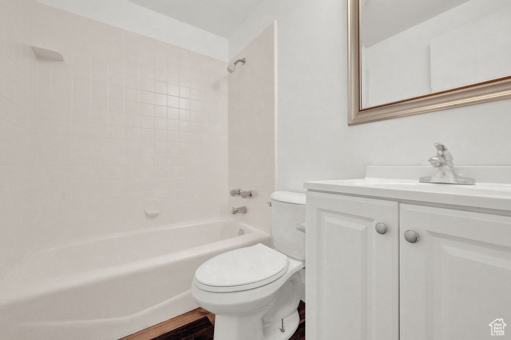 Full bathroom with hardwood / wood-style floors, vanity, tiled shower / bath combo, and toilet