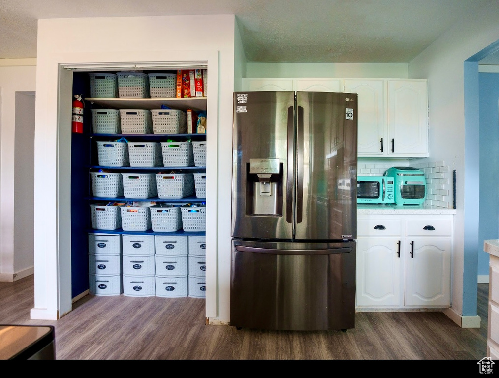 Kitchen featuring tasteful backsplash, dark wood-type flooring, white cabinetry, and stainless steel fridge