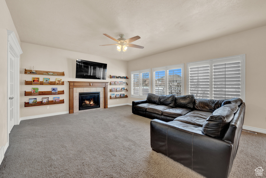 Living room featuring a tile fireplace, carpet floors, and ceiling fan