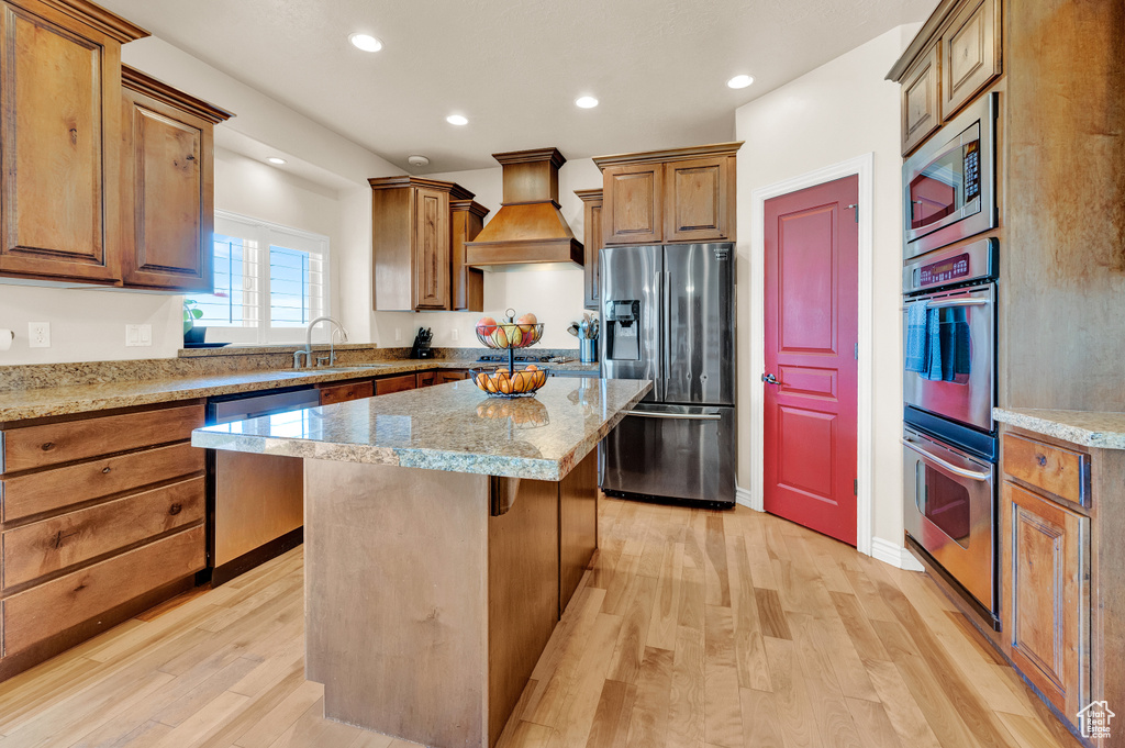 Kitchen with light wood-type flooring, appliances with stainless steel finishes, a kitchen island, and custom range hood