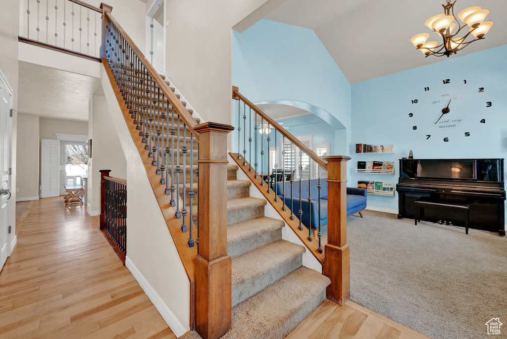 Staircase with a notable chandelier, light hardwood / wood-style floors, and high vaulted ceiling
