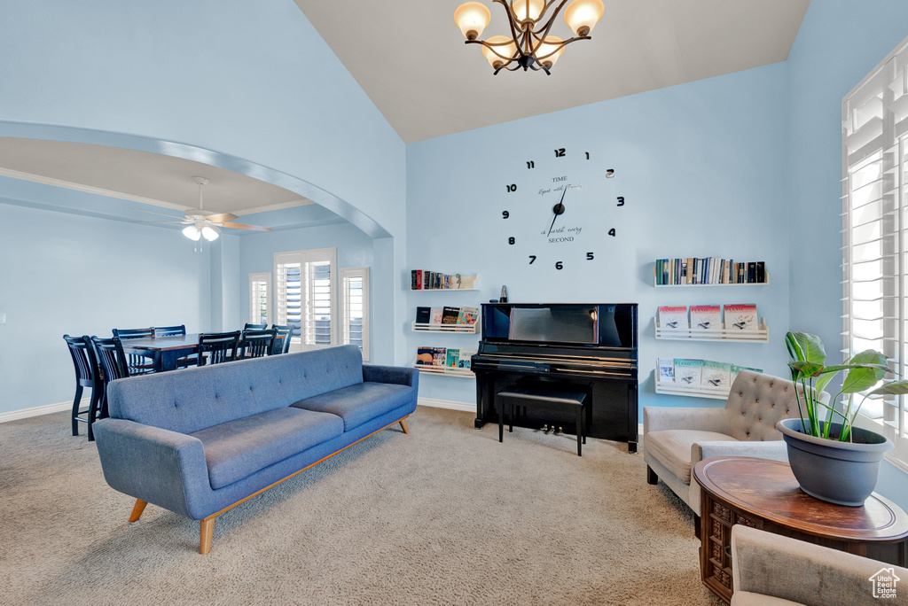 Carpeted living room featuring ceiling fan with notable chandelier and high vaulted ceiling