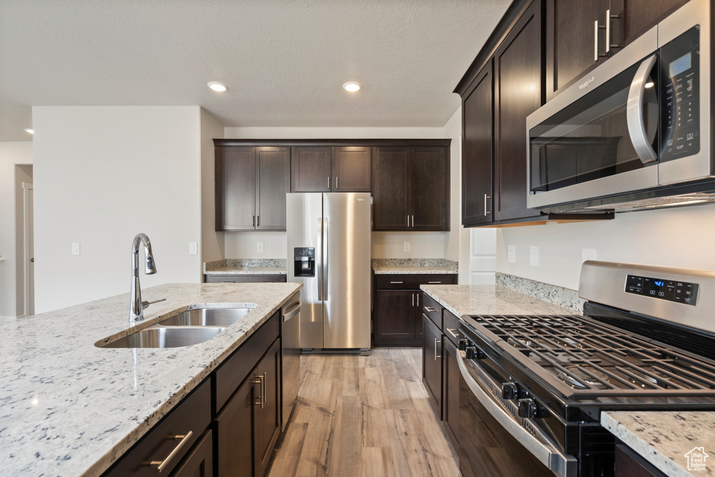 Kitchen featuring light hardwood / wood-style flooring, appliances with stainless steel finishes, dark brown cabinets, sink, and light stone counters