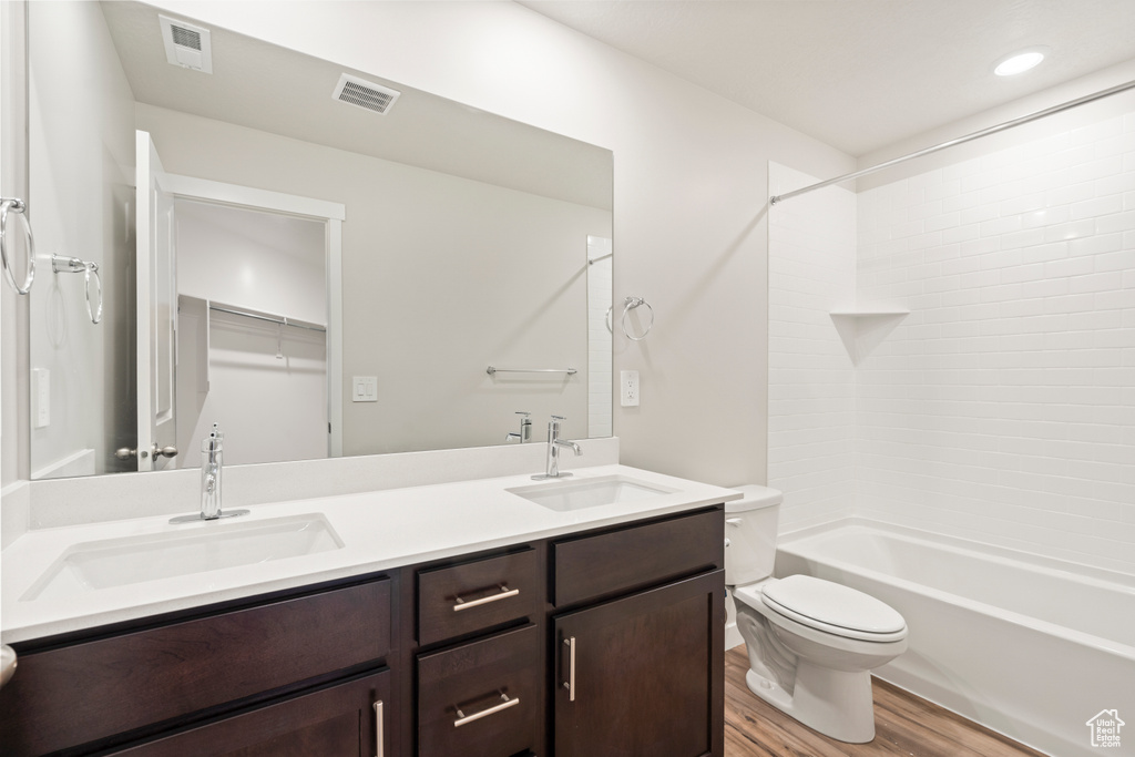 Full bathroom with tiled shower / bath, dual sinks, oversized vanity, toilet, and hardwood / wood-style flooring