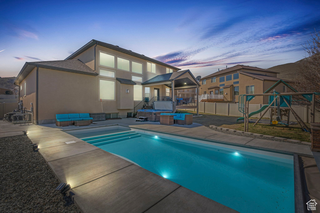 Pool at dusk with a playground, a patio area, a hot tub, and an outdoor living space