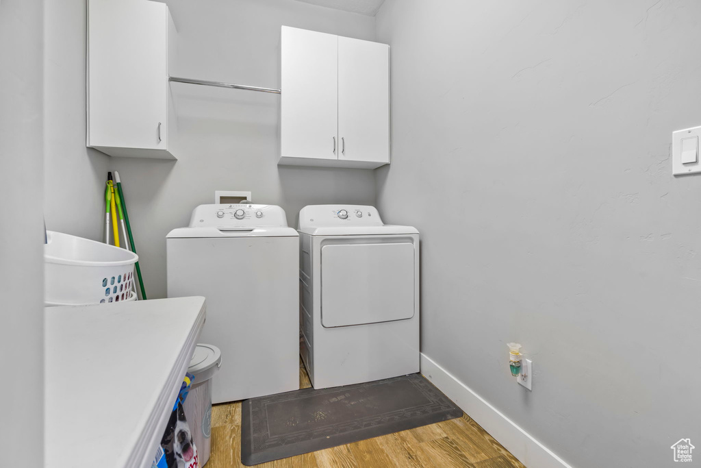 Washroom with cabinets, washer hookup, washing machine and dryer, and hardwood / wood-style flooring