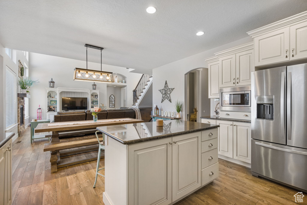 Kitchen featuring white cabinets, appliances with stainless steel finishes, a kitchen island, hanging light fixtures, and light hardwood / wood-style floors