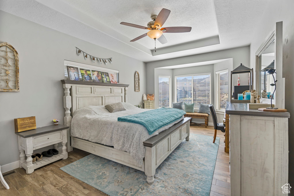 Bedroom with a raised ceiling, a textured ceiling, light wood-type flooring, and ceiling fan