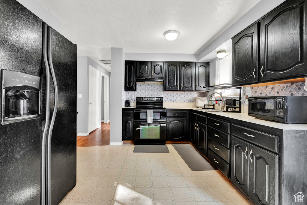 Kitchen with light tile flooring, black appliances, tasteful backsplash, and sink