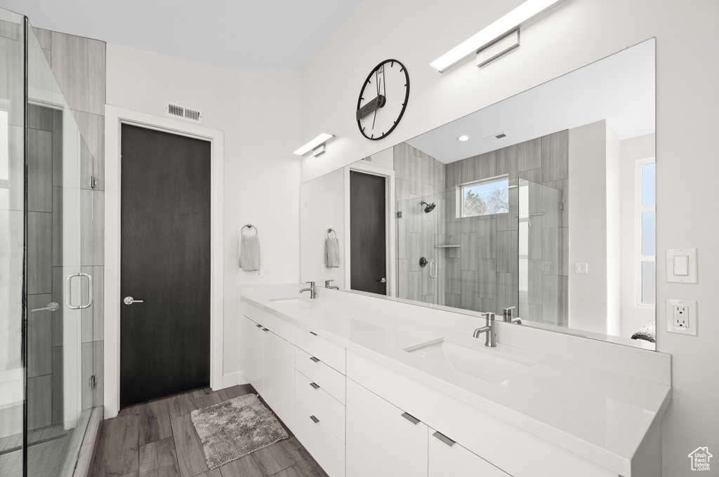 Bathroom featuring large vanity, a shower with shower door, dual sinks, and hardwood / wood-style flooring