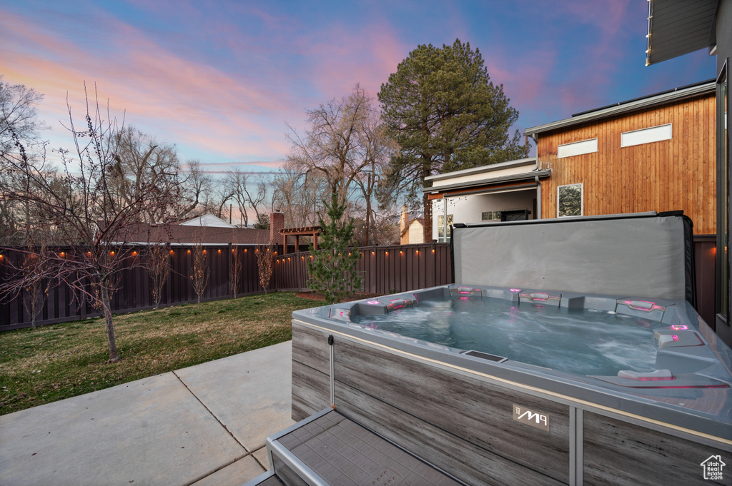 Patio terrace at dusk featuring a lawn and a hot tub