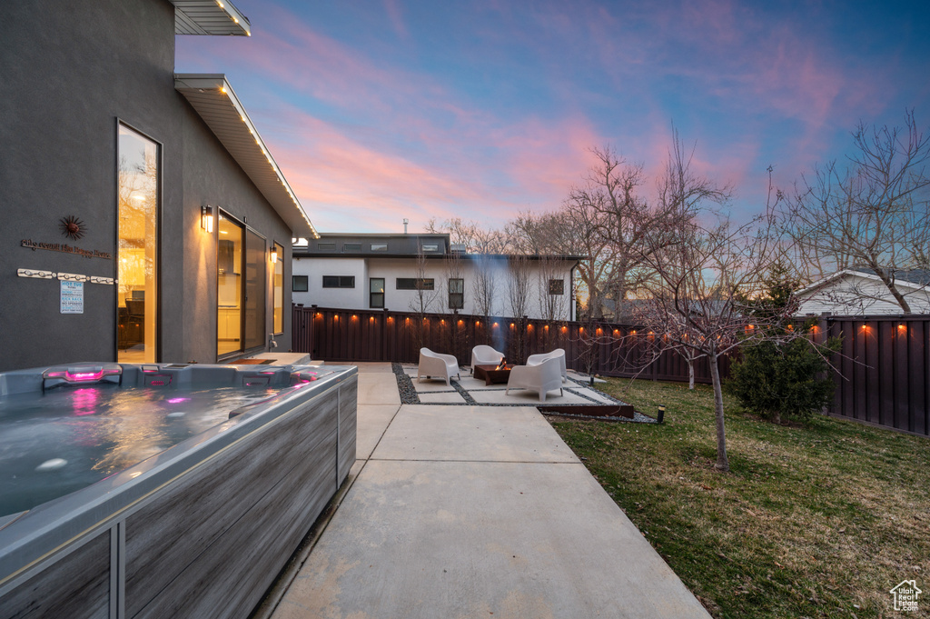 Patio terrace at dusk with an outdoor hangout area, a yard, and a hot tub