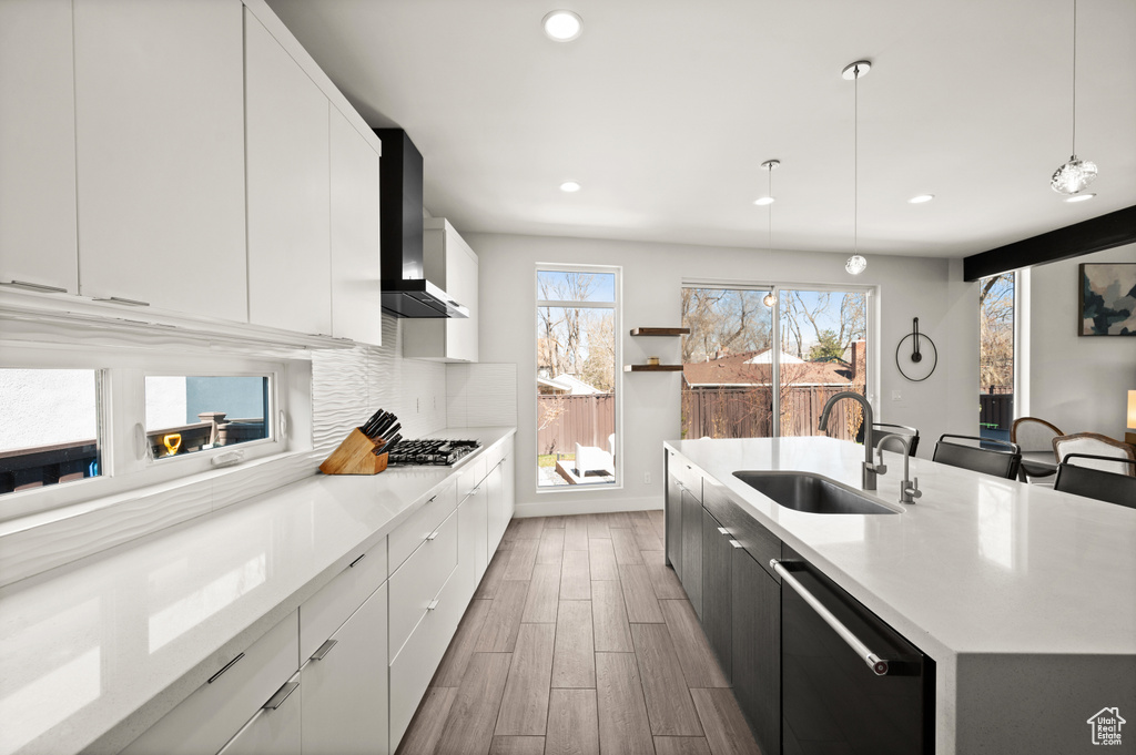 Kitchen with white cabinets, wall chimney range hood, pendant lighting, sink, and stainless steel dishwasher