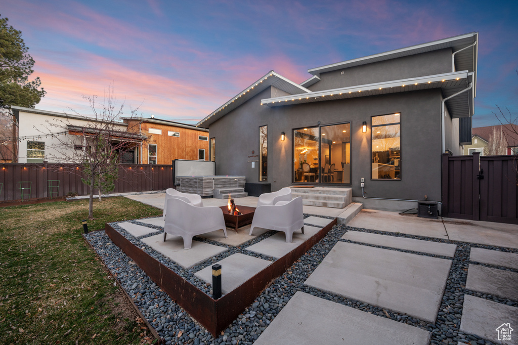 Back house at dusk featuring a patio area, a lawn, and an outdoor hangout area