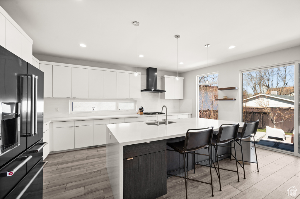 Kitchen featuring high quality fridge, wall chimney range hood, a kitchen island with sink, and a healthy amount of sunlight
