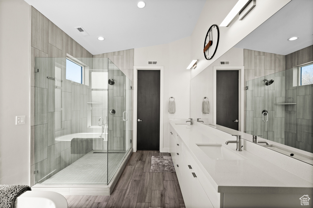 Bathroom with a shower with shower door, hardwood / wood-style flooring, dual sinks, and vanity with extensive cabinet space