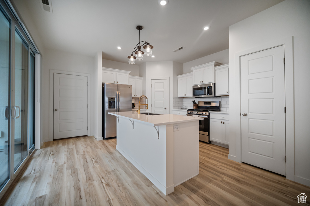 Kitchen featuring light wood-type flooring, a center island with sink, stainless steel appliances, a notable chandelier, and pendant lighting