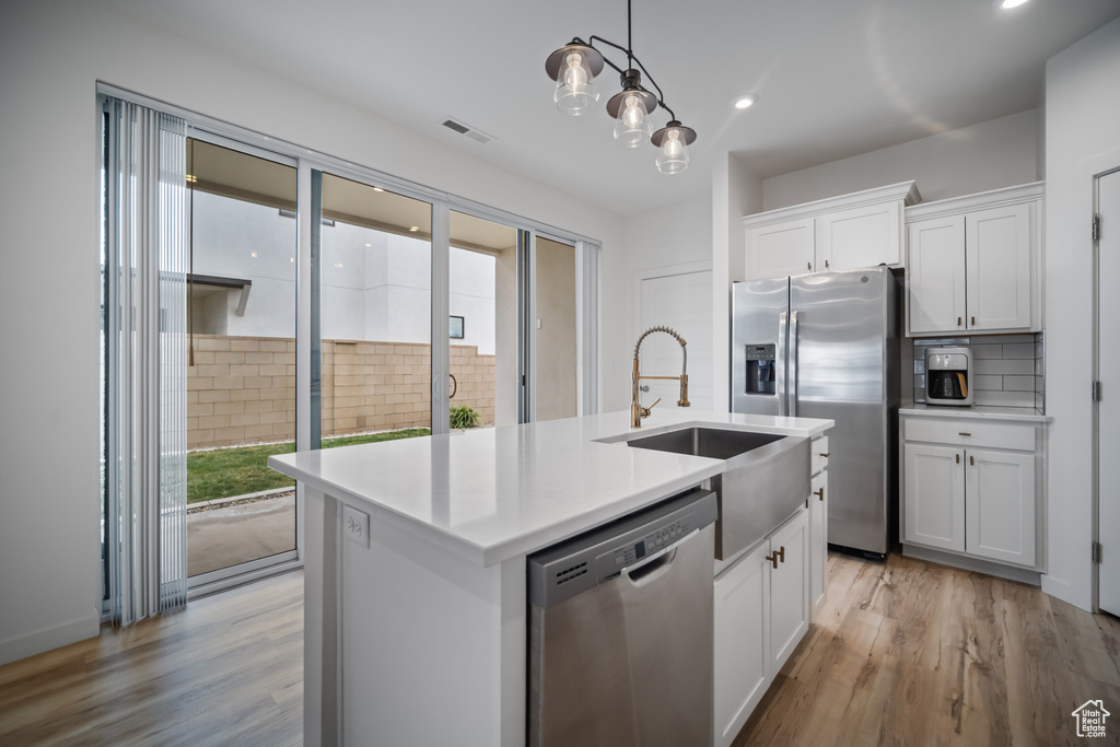 Kitchen featuring light hardwood / wood-style floors, appliances with stainless steel finishes, pendant lighting, and an island with sink
