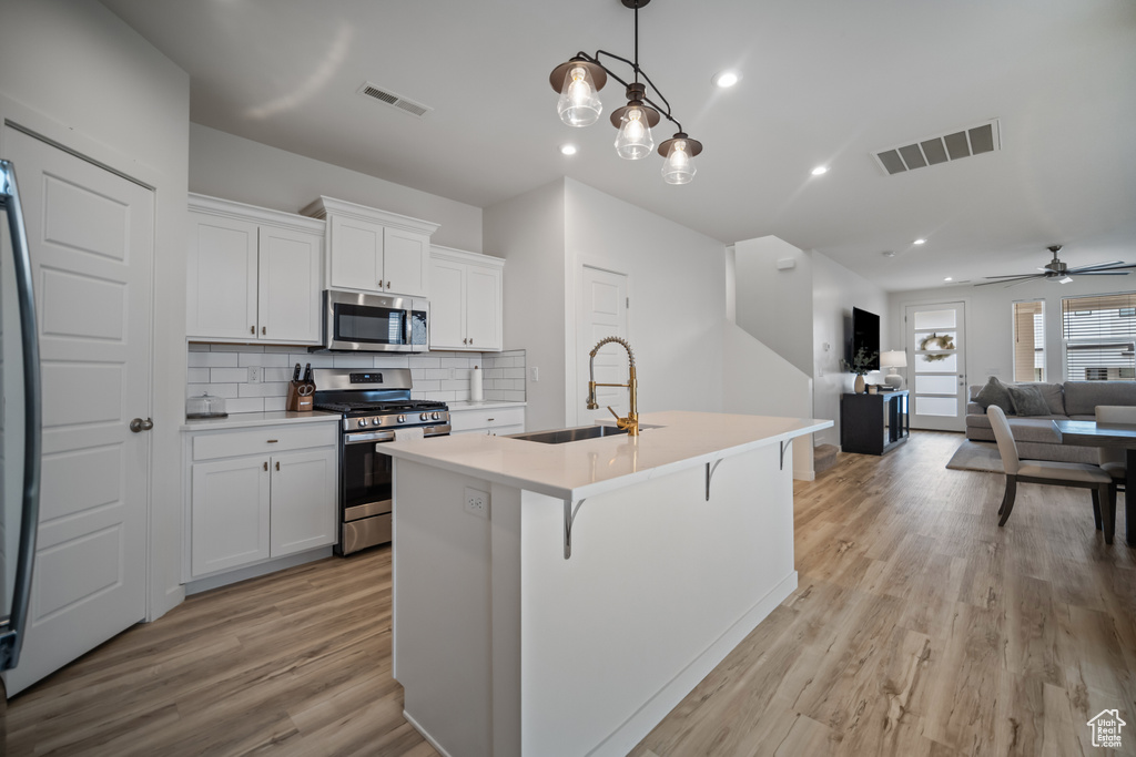 Kitchen featuring stainless steel appliances, sink, decorative light fixtures, ceiling fan with notable chandelier, and light hardwood / wood-style floors