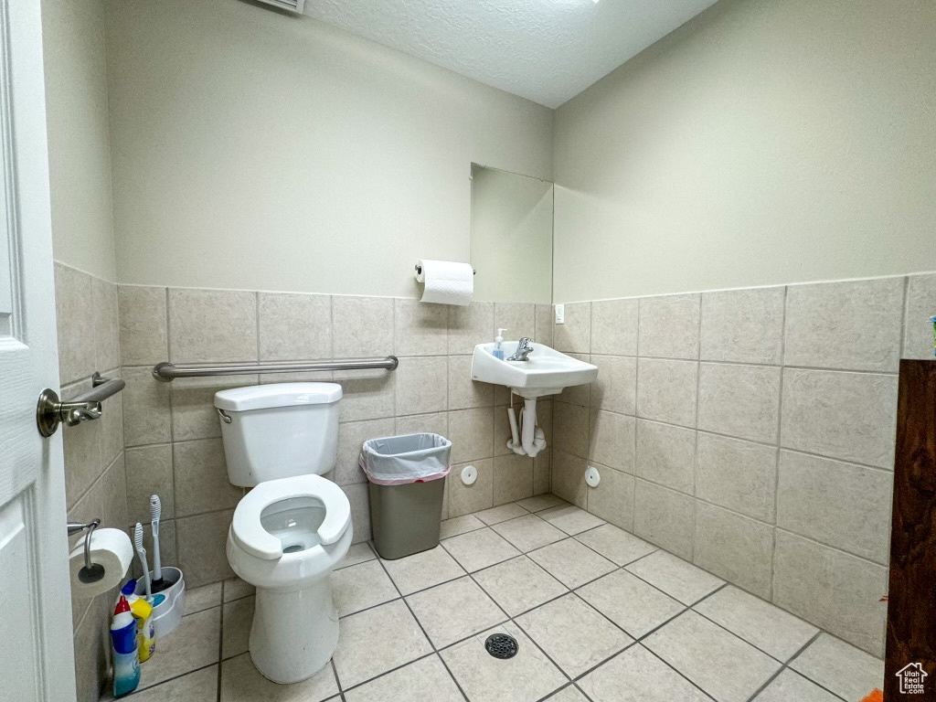 Bathroom with tile walls, tile floors, toilet, a textured ceiling, and sink