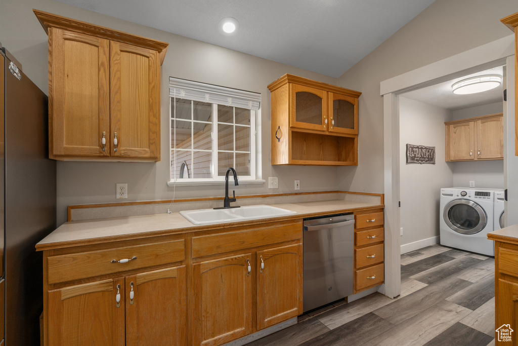 Kitchen with appliances with stainless steel finishes, washing machine and clothes dryer, wood-type flooring, sink, and vaulted ceiling