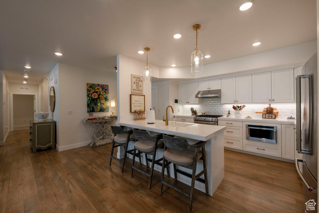 Kitchen with pendant lighting, appliances with stainless steel finishes, dark hardwood / wood-style flooring, white cabinetry, and backsplash