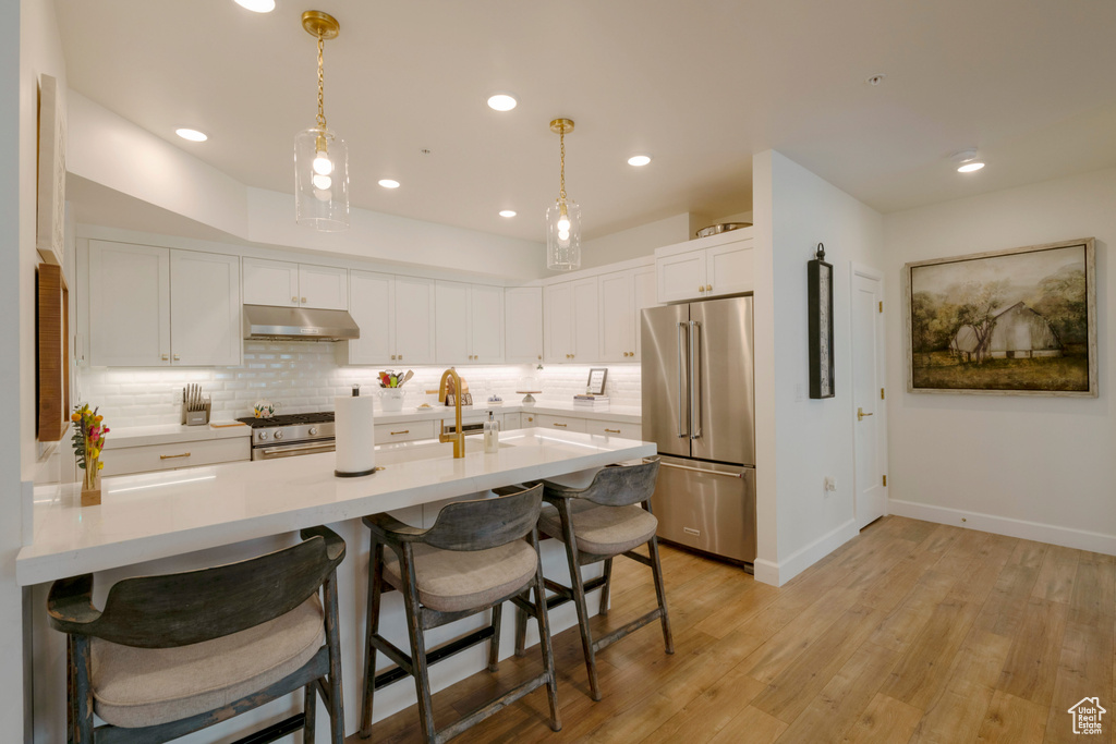 Kitchen featuring white cabinets, pendant lighting, high end appliances, and a kitchen bar