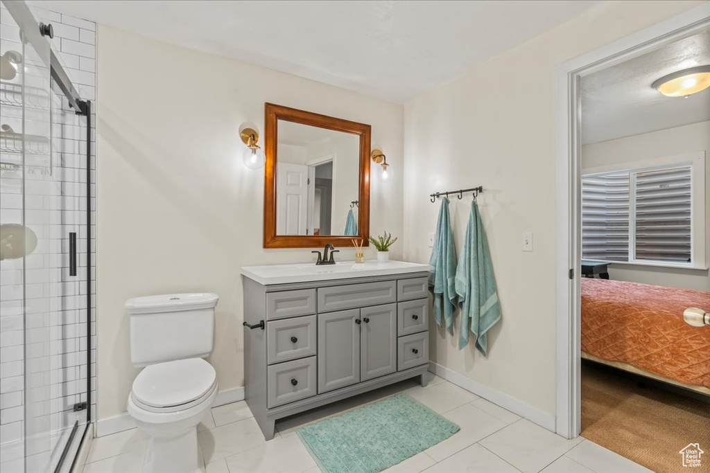 Bathroom featuring toilet, tile flooring, vanity with extensive cabinet space, and an enclosed shower