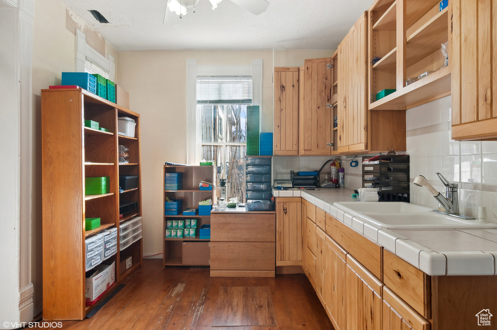 Kitchen with tile countertops, backsplash, ceiling fan, sink, and dark hardwood / wood-style flooring