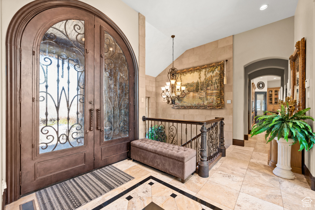 Entrance foyer featuring an inviting chandelier, vaulted ceiling, french doors, and light tile floors