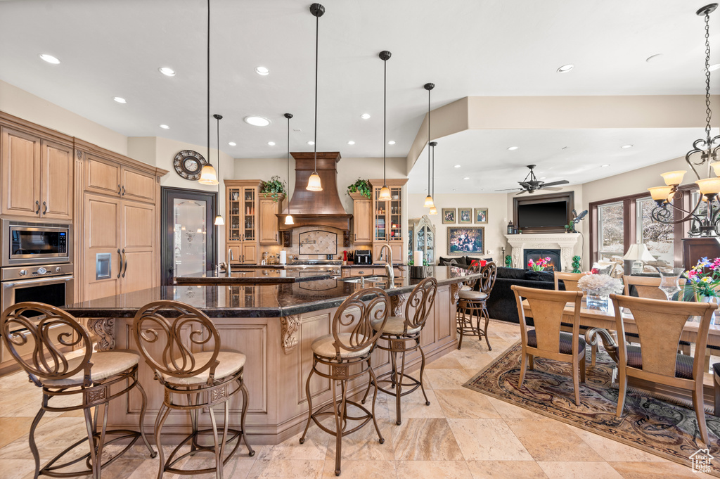 Kitchen featuring a breakfast bar area, pendant lighting, ceiling fan with notable chandelier, and custom range hood
