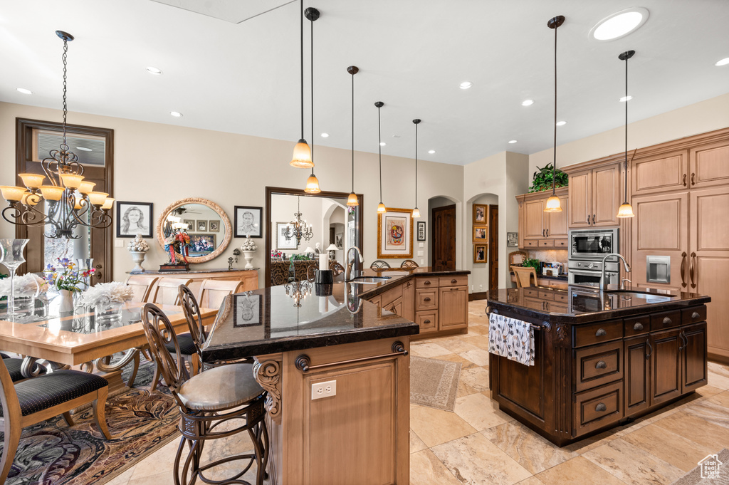 Kitchen with a large island, appliances with stainless steel finishes, a notable chandelier, hanging light fixtures, and a kitchen bar