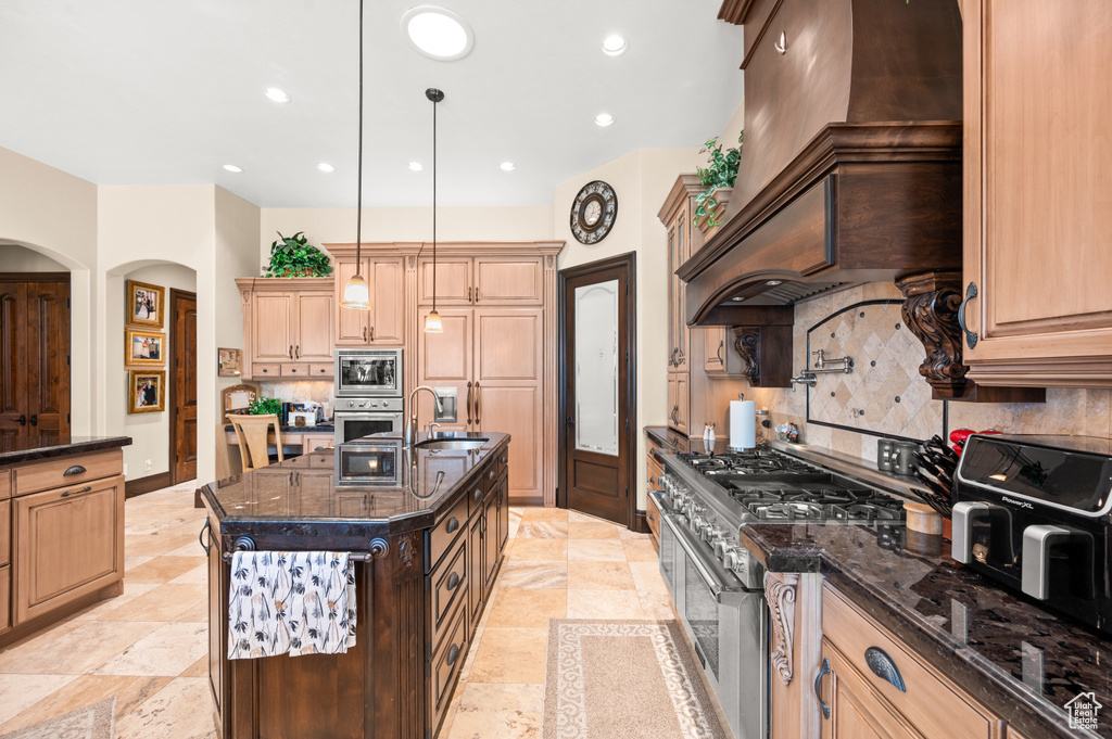 Kitchen with backsplash, a kitchen island with sink, appliances with stainless steel finishes, and custom range hood