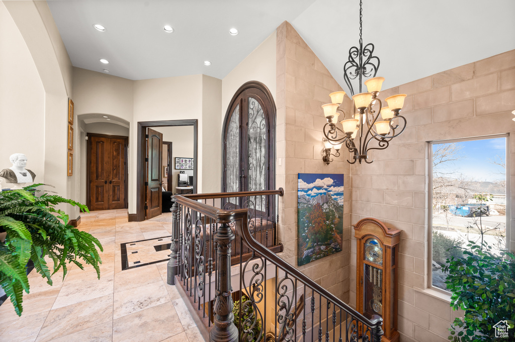 Hallway featuring tile walls, an inviting chandelier, and light tile flooring