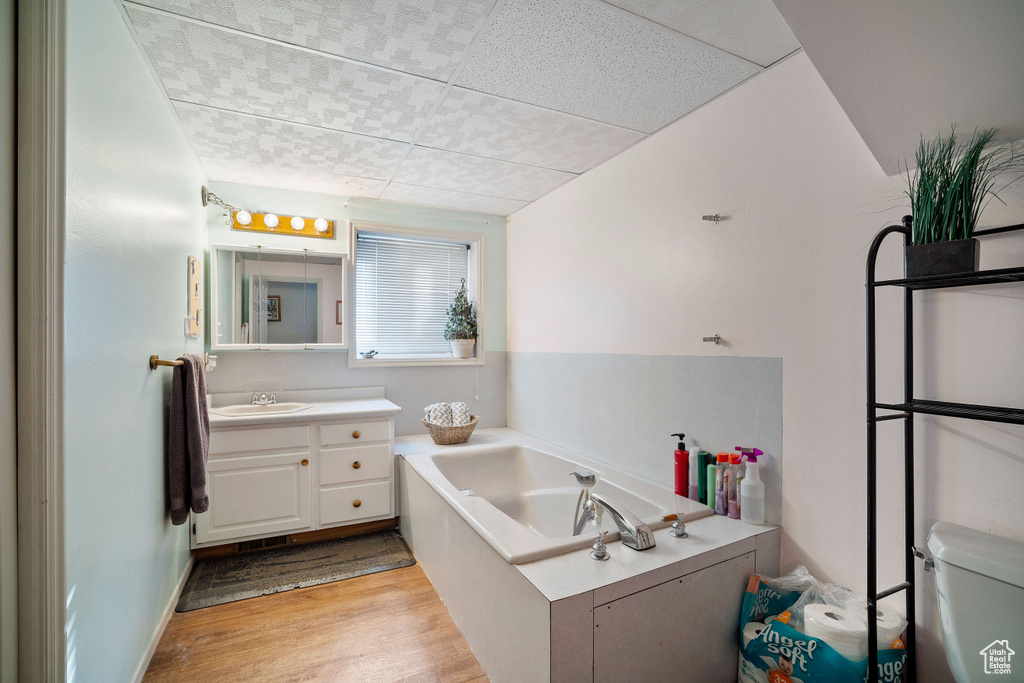Bathroom featuring vanity, hardwood / wood-style flooring, a tub, a drop ceiling, and toilet