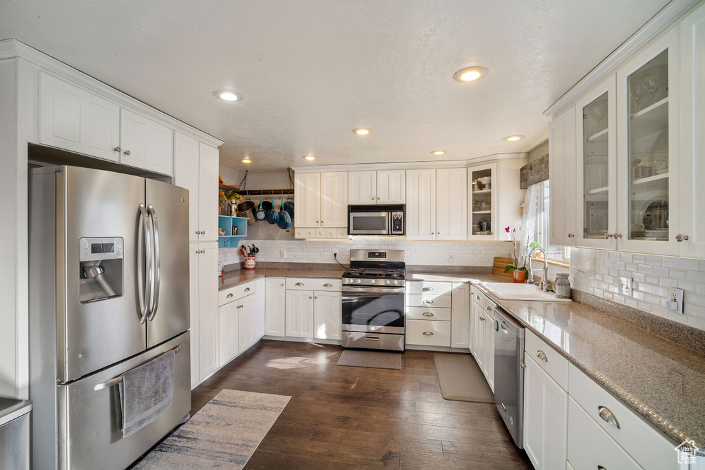 Kitchen with dark hardwood / wood-style floors, white cabinets, sink, stainless steel appliances, and tasteful backsplash