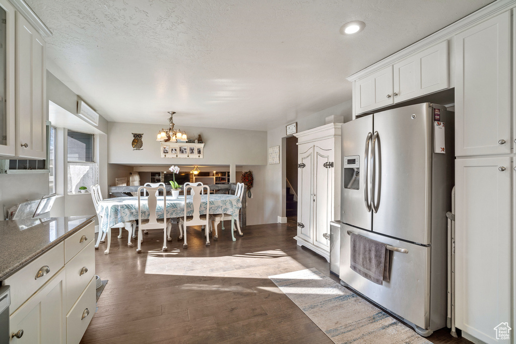 Kitchen with white cabinets, decorative light fixtures, a notable chandelier, stainless steel fridge with ice dispenser, and dark hardwood / wood-style flooring