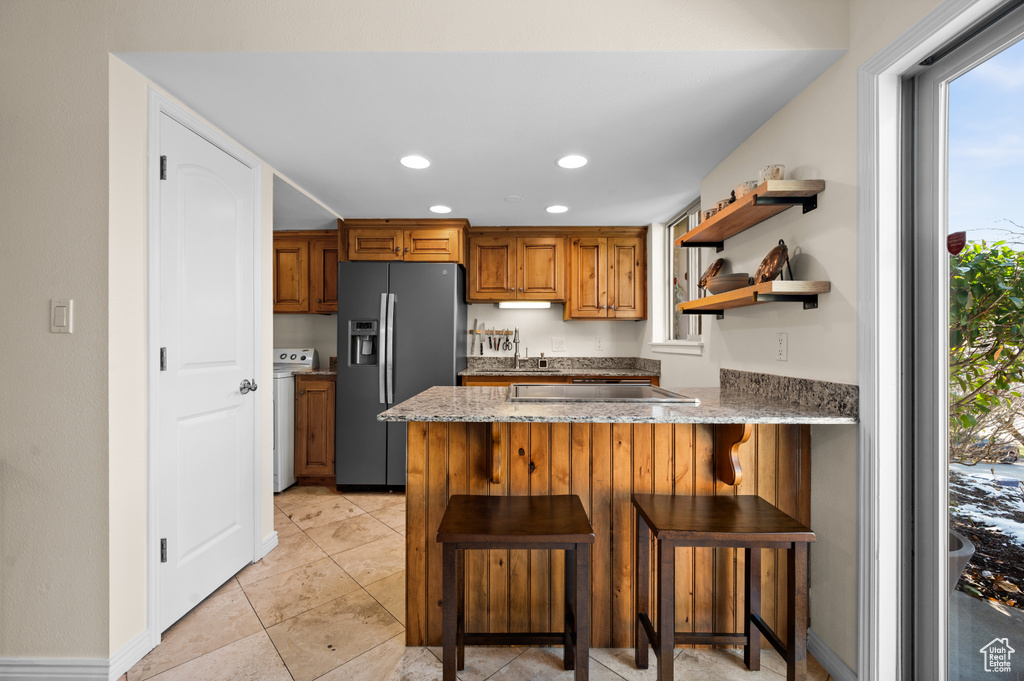 Kitchen with a kitchen breakfast bar, plenty of natural light, light tile flooring, and stainless steel fridge with ice dispenser