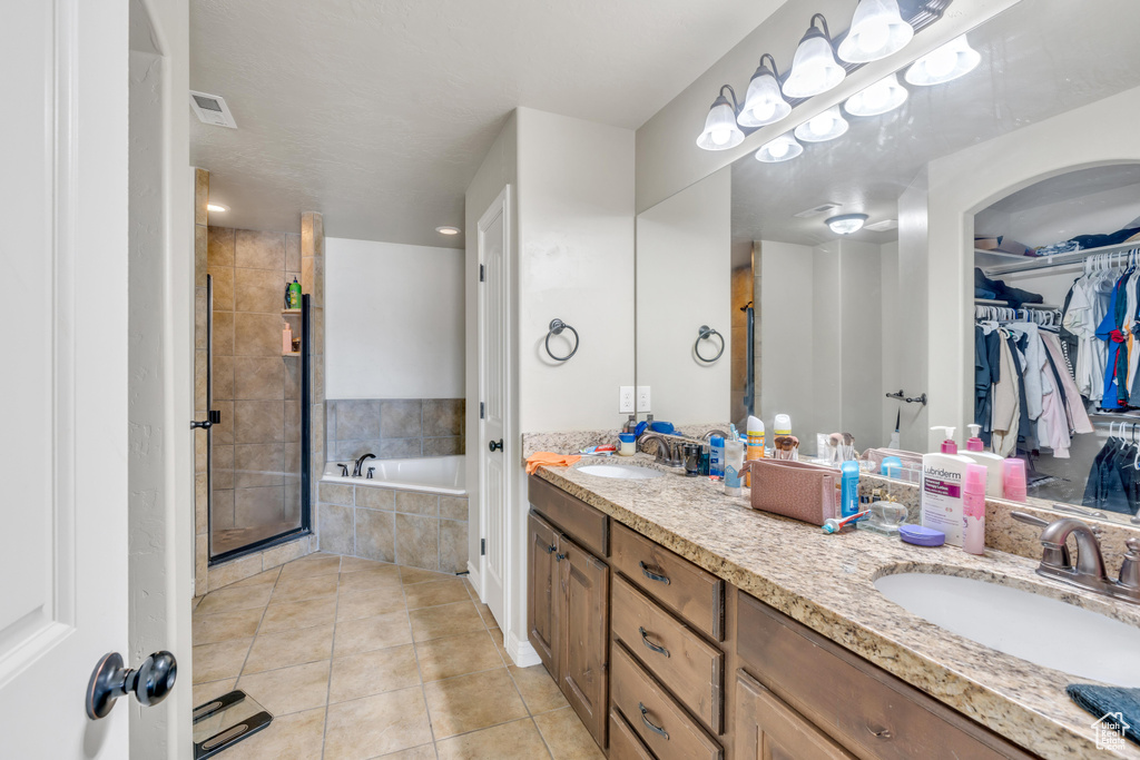 Bathroom featuring vanity with extensive cabinet space, double sink, tile flooring, and plus walk in shower