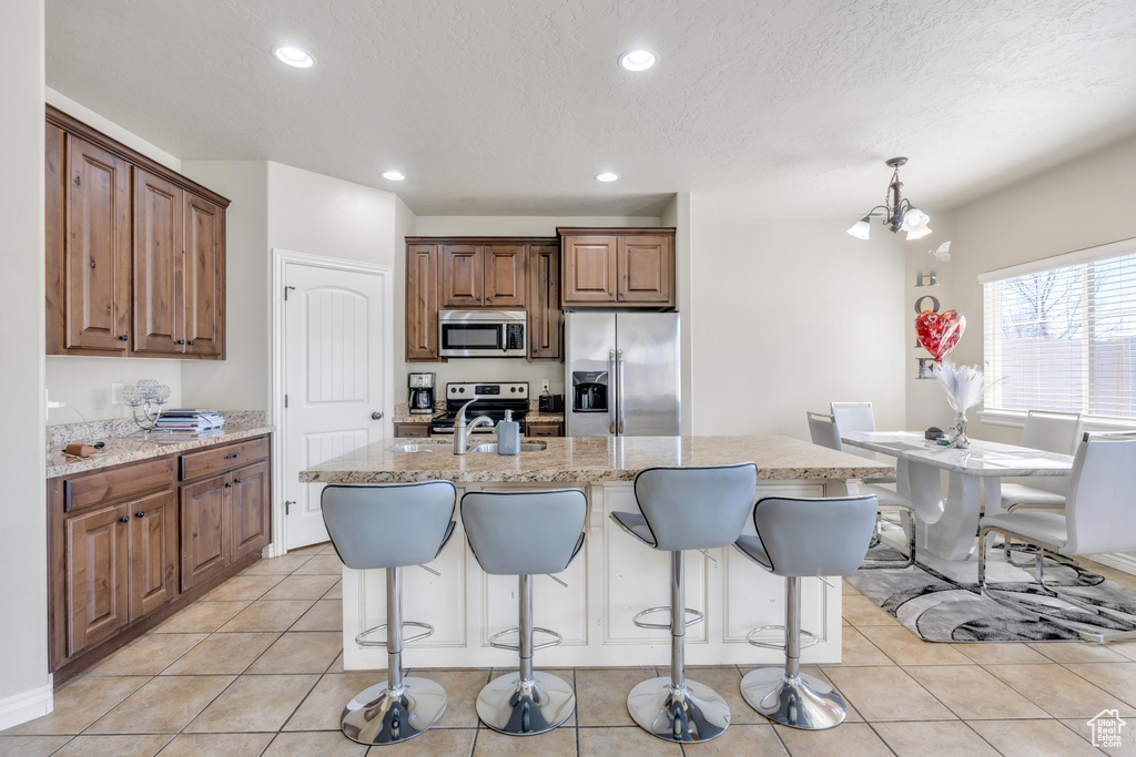 Kitchen featuring a notable chandelier, pendant lighting, appliances with stainless steel finishes, an island with sink, and light tile floors