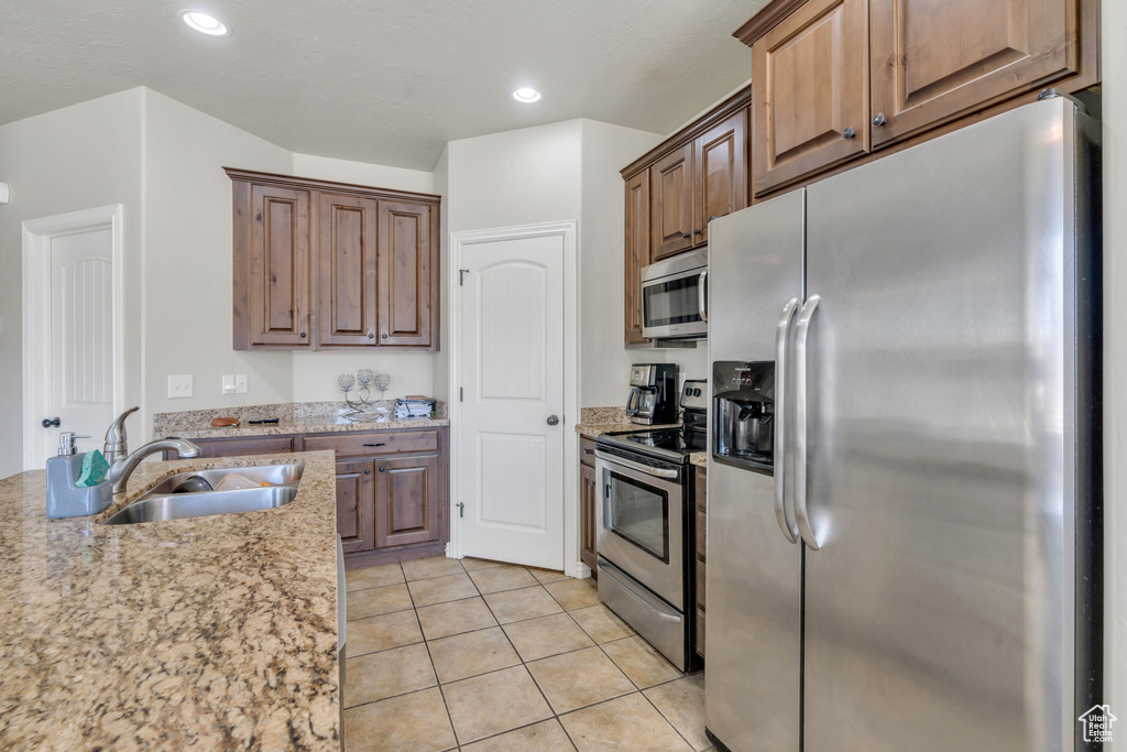 Kitchen featuring light stone countertops, light tile floors, sink, and stainless steel appliances