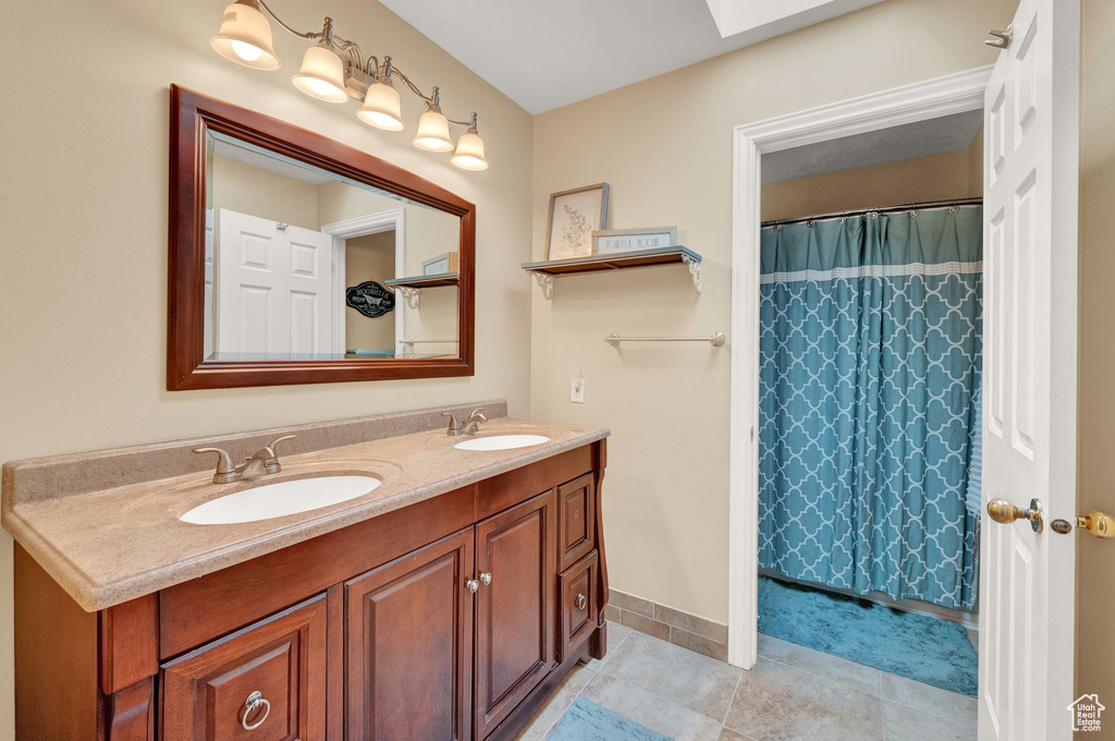 Bathroom with a skylight, tile flooring, large vanity, and dual sinks