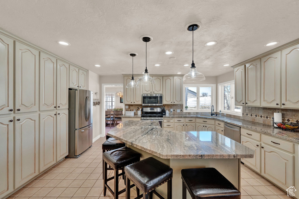 Kitchen with decorative light fixtures, stainless steel appliances, a breakfast bar, and a center island