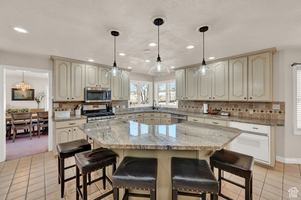 Kitchen featuring light tile floors, tasteful backsplash, stainless steel appliances, and decorative light fixtures