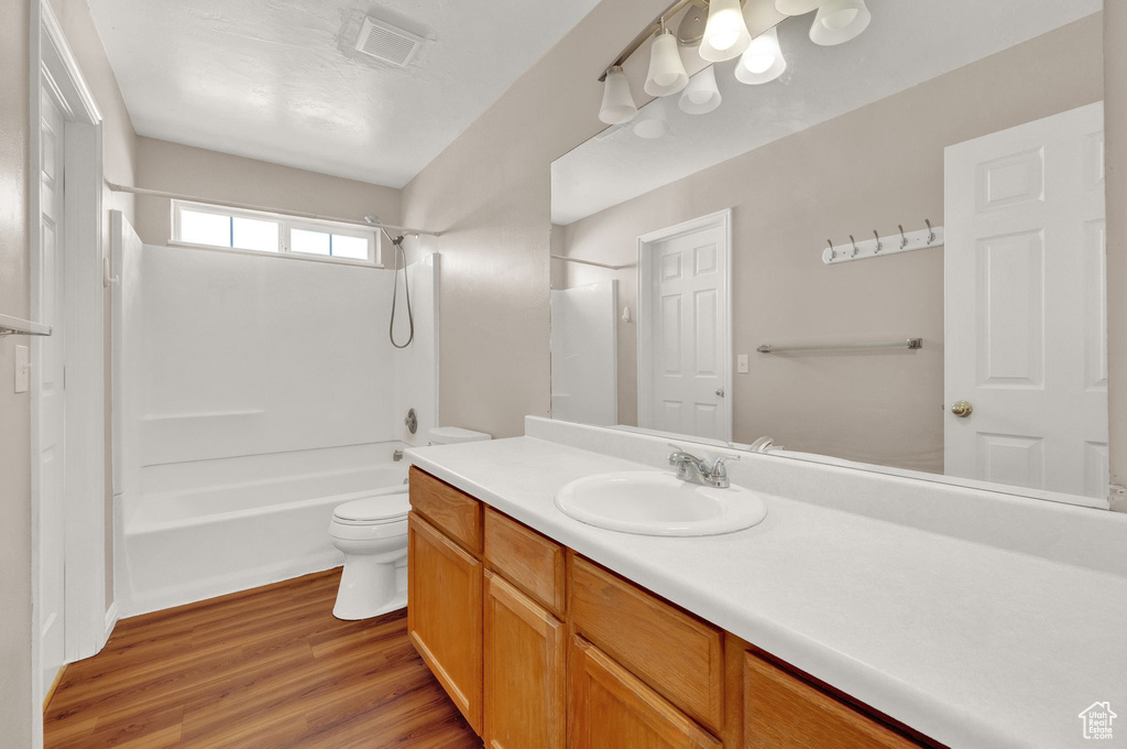Full bathroom featuring wood-type flooring, shower / tub combination, toilet, and vanity with extensive cabinet space