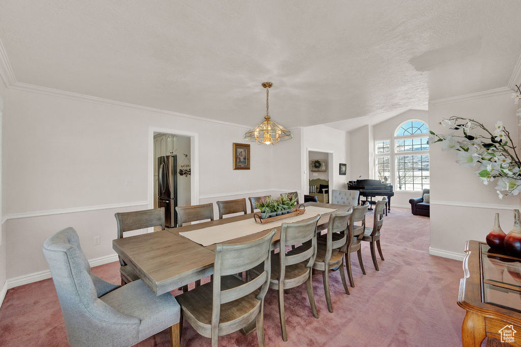 Dining space featuring a notable chandelier, lofted ceiling, crown molding, and light colored carpet