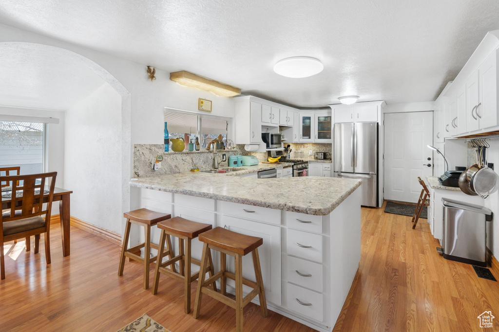 Kitchen featuring kitchen peninsula, stainless steel appliances, tasteful backsplash, and light hardwood / wood-style floors