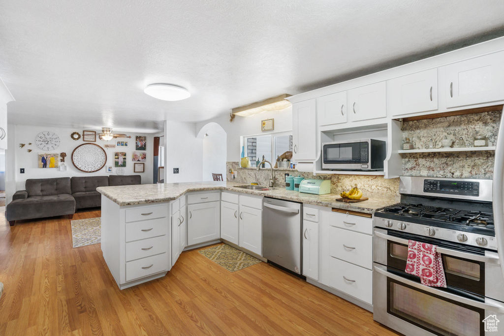 Kitchen featuring backsplash, kitchen peninsula, stainless steel appliances, and light wood-type flooring