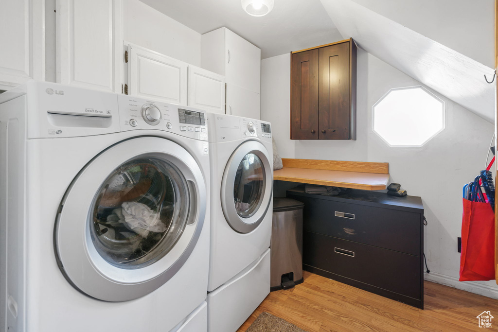 Washroom with light hardwood / wood-style floors, washer and dryer, and cabinets