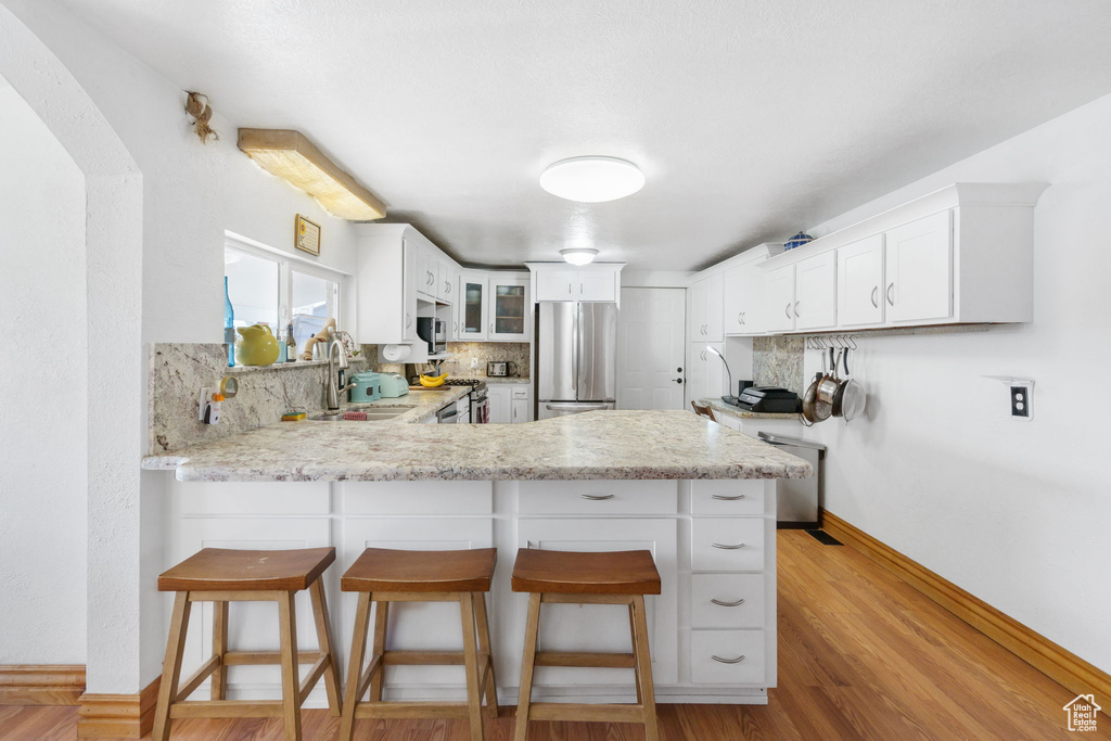 Kitchen featuring stainless steel appliances, tasteful backsplash, white cabinetry, kitchen peninsula, and light hardwood / wood-style floors